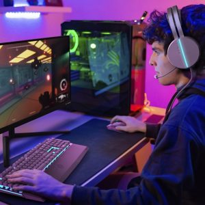 Caucasian young teenager plays computer in his room with colored lights and looks at the screen concentrated